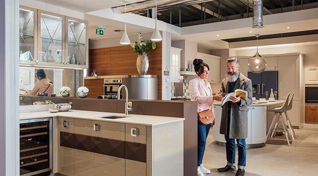 A man and woman discussing a brochure in a modern kitchen showroom with sleek cabinets and industrial elements.