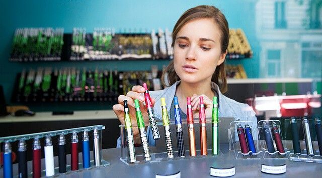 A vape store owner examining a red vape in a well-organized store. Various products are on the shelves in the background.