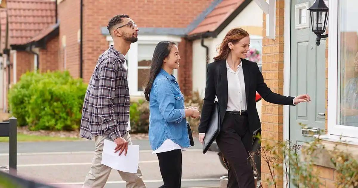 Three individuals, including a landlord and two tenants, walk together, looking at a house on the market.