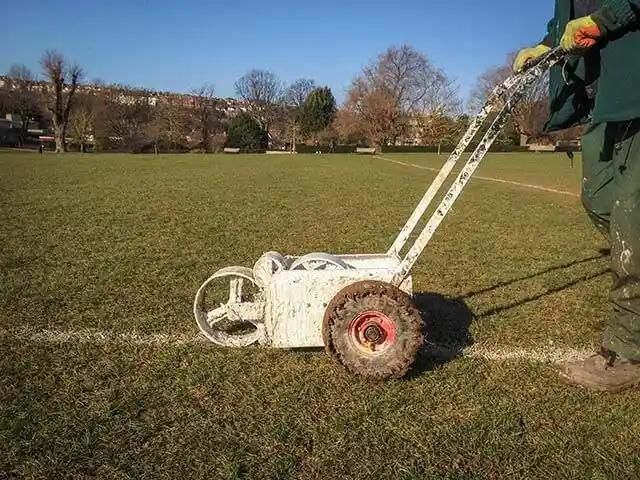 Person marking a football pitch with a line marking machine on a grass field.