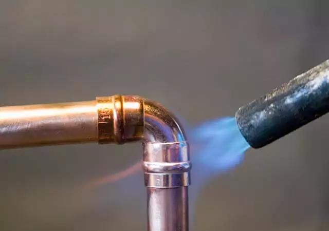 Blowtorch welding a copper pipe joint with a blue flame.