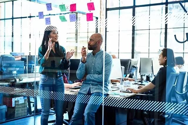 Two IT consultants in a modern office having a meeting with sticky notes on the glass wall in front of them.