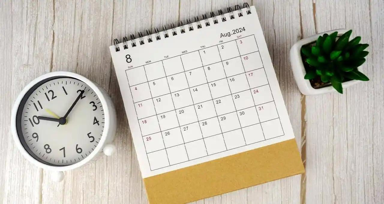 Calendar on a wooden table beside a clock and a small green plant, creating a serene workspace atmosphere.