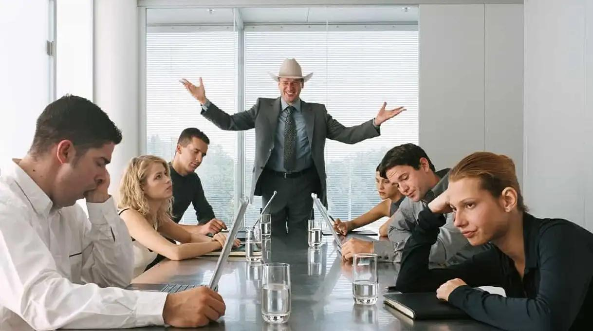 A person stood at the front of a meeting room with meeting attendees looking disinterested.