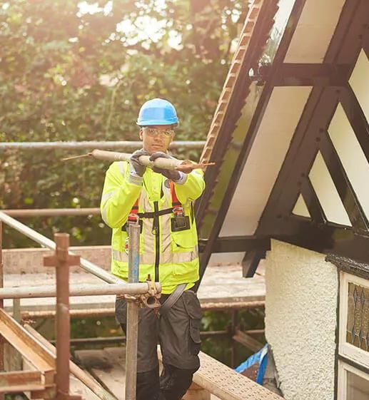 A construction worker carrying a metal pole on scaffolding beside a building.