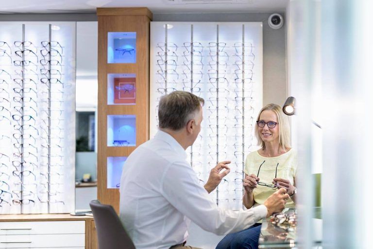 Woman holding glasses while consulting with an optician in an eyeglass shop.