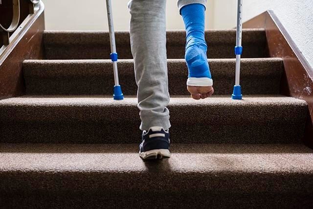 Person with blue cast on crutches ascending a staircase, wearing sweatpants and a trainer on their left foot.