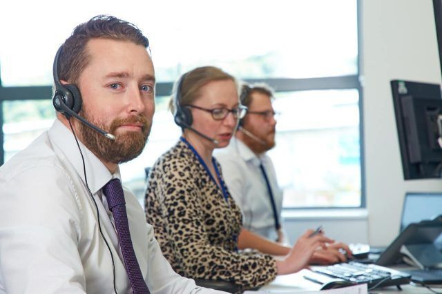 Two men and a woman with headsets on in an office setting, likely participating in a discussion or online call.