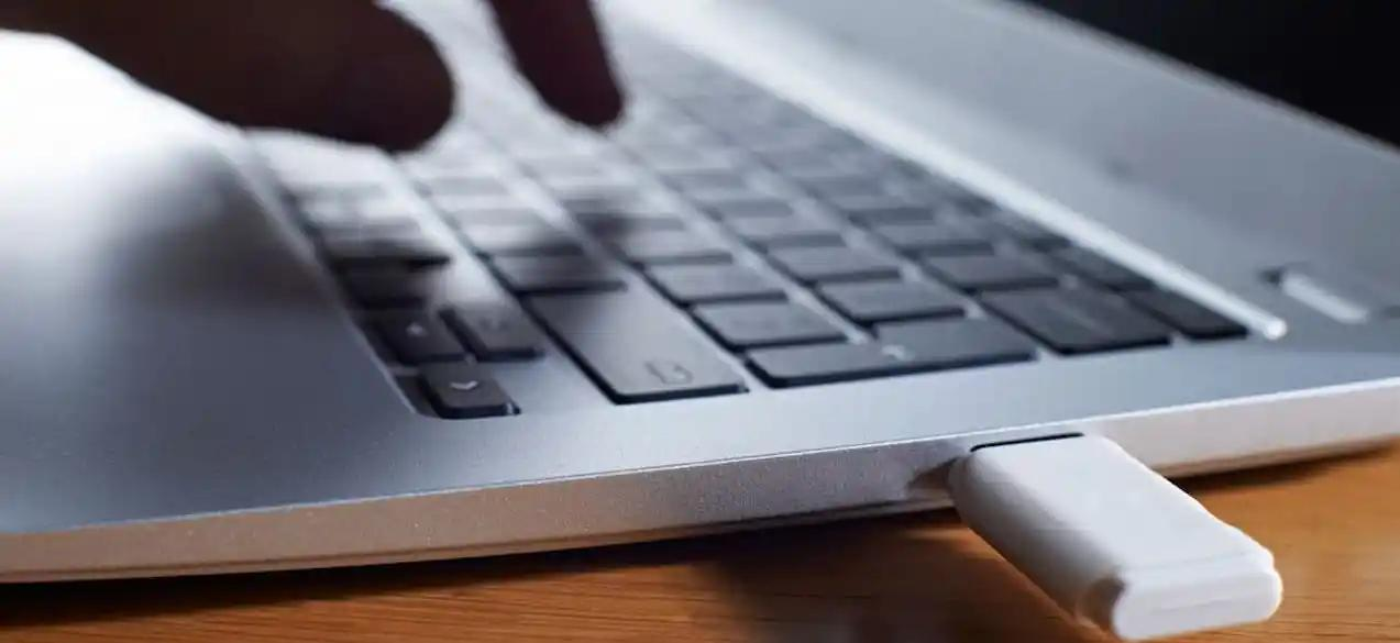 A hand is connecting a small white USB stick to a laptop.