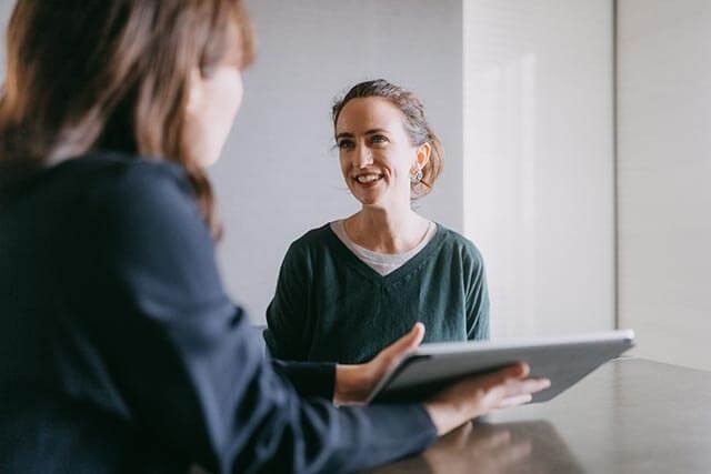 Web designer showing a tablet to a client in a bright office or meeting space.