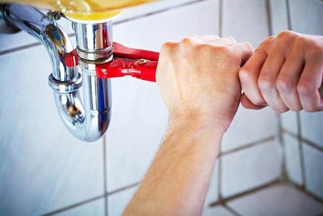 A close-up at the hands of a plumber using a wrench under a toilet sink.