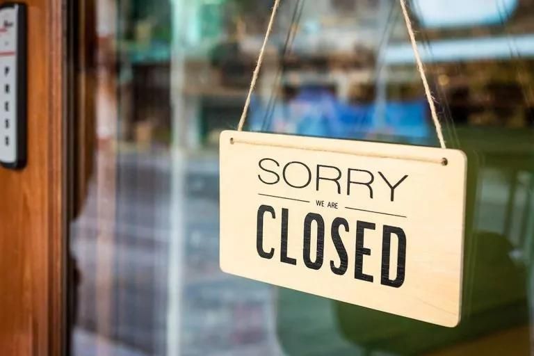 Close-up of a “Sorry, We’re Closed” sign hanging on a glass door with a blurred indoor background.