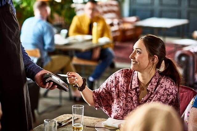 Woman seated at a table paying a restaurant bill with a card.