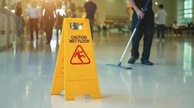 Caution Wet Floor sign on a shiny floor with a person mopping in the background.