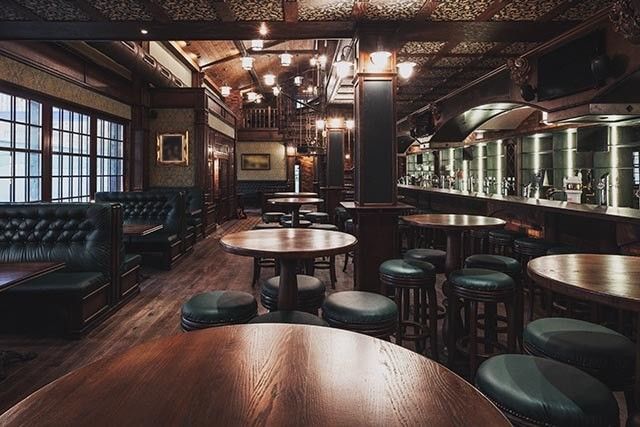Interior of a bar showcasing rustic wooden tables and stools, with a warm and inviting atmosphere.