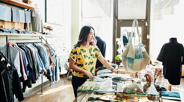 a fashion retail store worker is arranging items in a boutique while sunlight streaming through the windows.