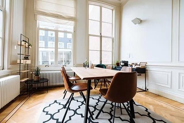 Modern meeting room with a wooden dining table, brown chairs, large windows, and a black-and-white rug.