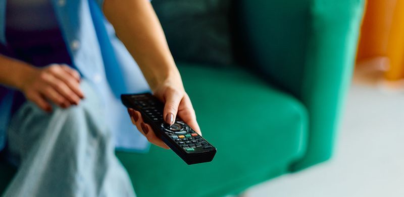 Person sat on a green sofa pointing a television remote control