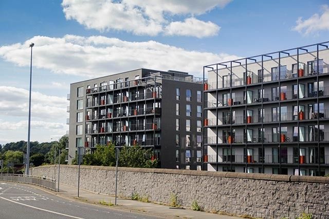 Modern student buildings with glass balconies surrounded by a brick wall and some greenery.