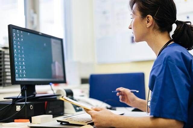 A nurse or doctor in scrubs looking at a computer screen while checking patient information.