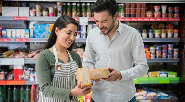 Woman and man smiling in a grocery store aisle, holding packaged food items with stocked shelves.