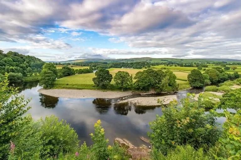 Scenic view of a winding river with green fields and distant hills under a cloudy sky.