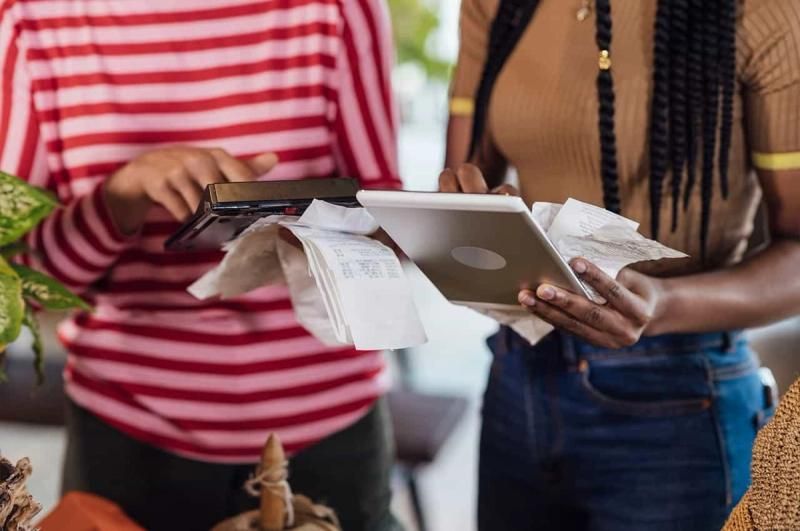 Close up or two people holding receipts and looking at a tablet device