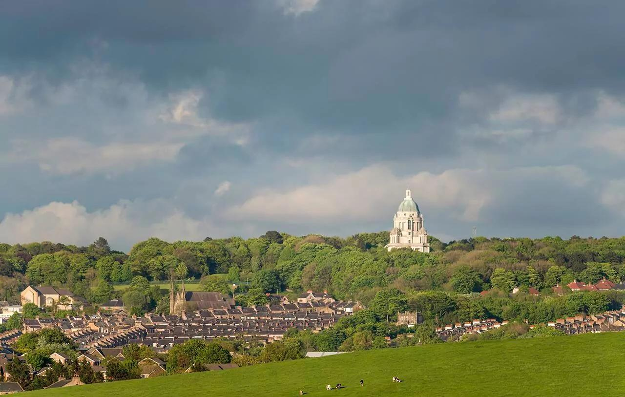 View of Lancaster with Ashton Memorial and grassy field, under a cloudy sky.