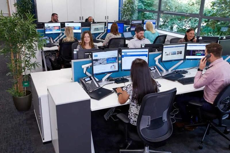 Group of office insurance brokers sat at their desks, in a brightly lit workspace. Some are engaging with computers or phones.