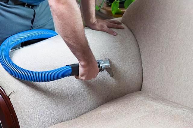 A cleaner is cleaning a beige sofa with a blue upholstery tool.