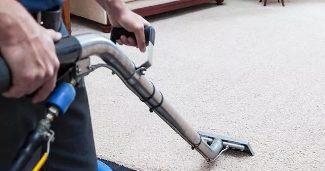 Person using a carpet cleaning machine on a light-coloured carpet.
